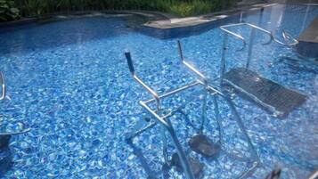 A swimming pool with clear blue water, metal pool chairs, and a tiled deck.