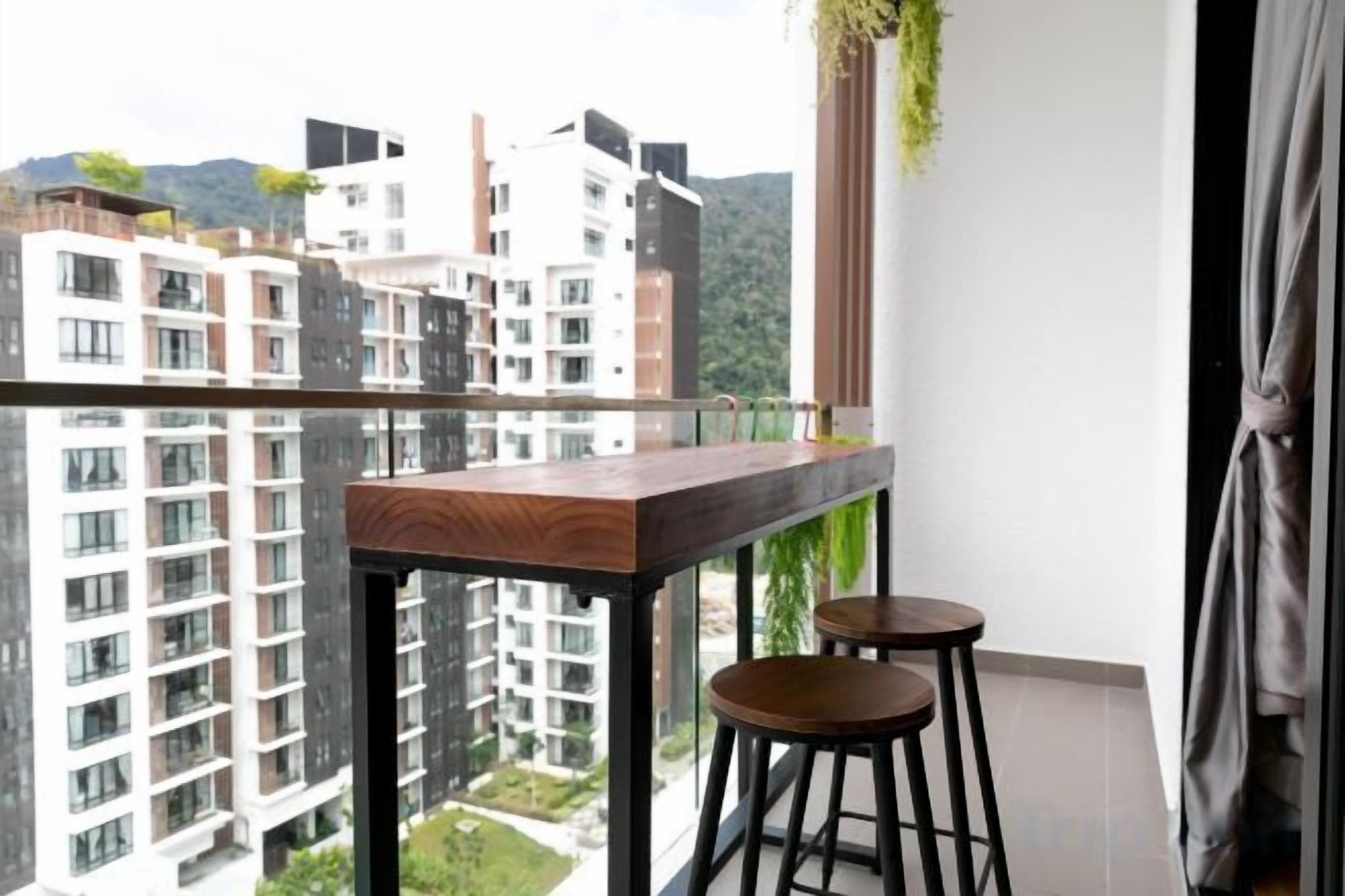 A balcony with a wooden table and two stools, overlooking a residential area with high-rise buildings.