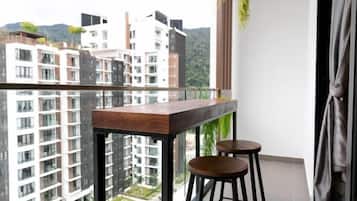 A balcony with a wooden table and two stools, overlooking a residential area with high-rise buildings.