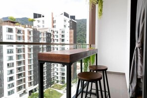 Un balcón con una mesa de madera y dos taburetes, con vista a una zona residencial con edificios altos.