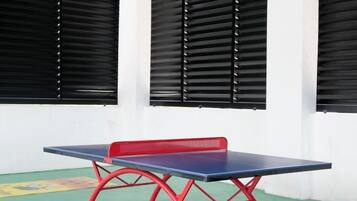 A ping pong table with a red frame, positioned in front of a wall with three black window blinds.