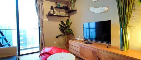 Un salon moderne avec une grande télévision, un canapé, une petite table ronde et une plante.