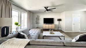 A modern living room with a sofa, a coffee table, a television, and a ceiling fan. - Ultimate Sports & Relaxation Retreat – Private Courts & Large Yard (Nampa)