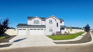 A two-story house with a garage, a well-maintained lawn, and a clear blue sky. - Ultimate Sports & Relaxation Retreat – Private Courts & Large Yard (Nampa)