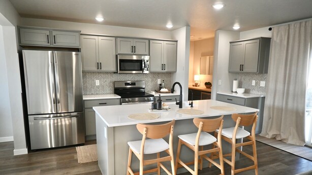 A modern kitchen with stainless steel appliances, a central island with bar stools, and light grey cabinetry. - Ultimate Sports & Relaxation Retreat – Private Courts & Large Yard (Nampa)