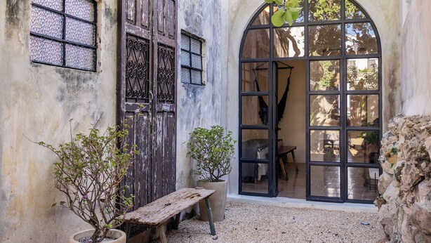 A rustic building with a large arched window, a wooden bench, and potted plants. - Casa Toto - Centro Luxe Retreat  (Mérida)