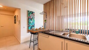 A modern kitchen with a black countertop, stainless steel sink, and a wooden slatted partition.