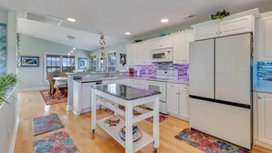 A modern kitchen with white cabinets, a central island, and a large refrigerator. - Just Chillin' (Kure Beach)