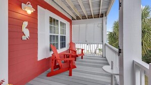 A covered porch with red Adirondack chairs, white shutters, and a small table. - Just Chillin' (Kure Beach)