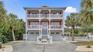 A two-story building with a central staircase, a red and white color scheme, and a white fence surrounding the property. - Just Chillin' (Kure Beach)