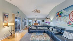 A modern living room with a sectional sofa, a coffee table, and a large beach-themed mural. - Just Chillin' (Kure Beach)