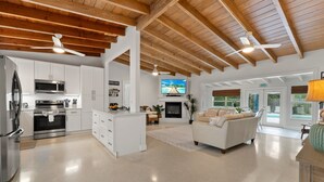 A spacious living area with a kitchen, white cabinetry, a fireplace, and a large window. - Paradise Palms, Private backyard w/ Pool, Hot tub! (Stuart)