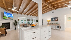 A spacious living area with a large white island, wooden ceiling beams, a fireplace, and a television. - Paradise Palms, Private backyard w/ Pool, Hot tub! (Stuart)