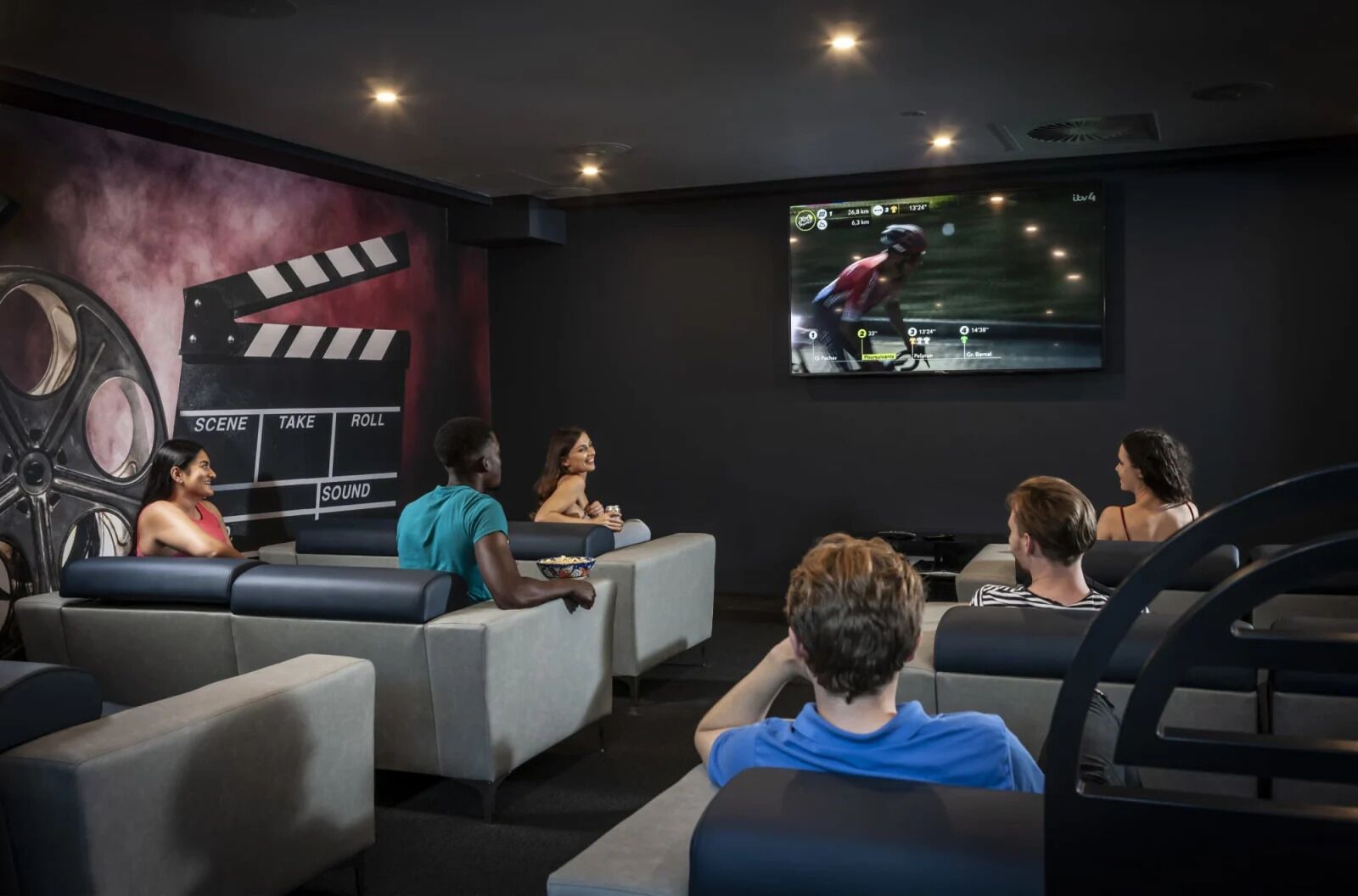 Une salle de cinéma dotée de sièges inclinables et d’un grand écran diffusant une course cycliste.
