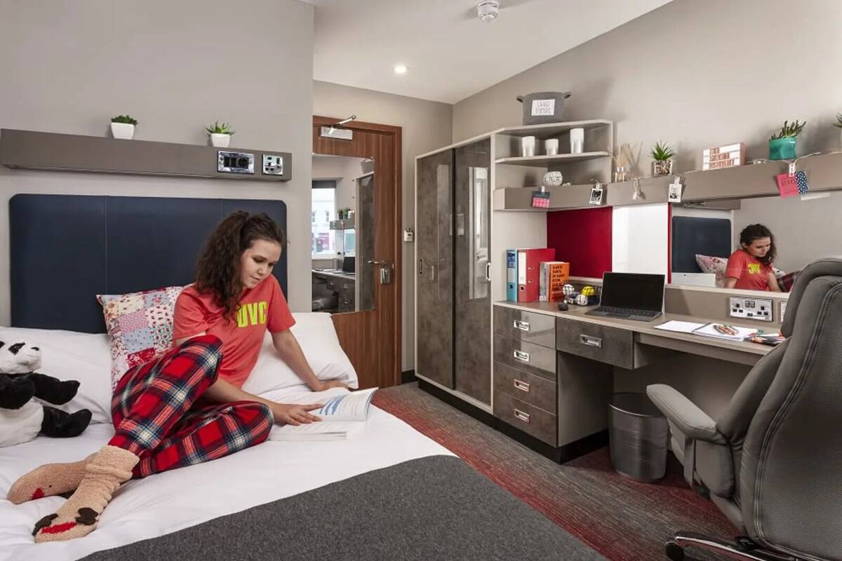 Ett modernt hotellrum med en säng, ett skrivbord och en stol. På sängen ligger en mjukdjurspanda.