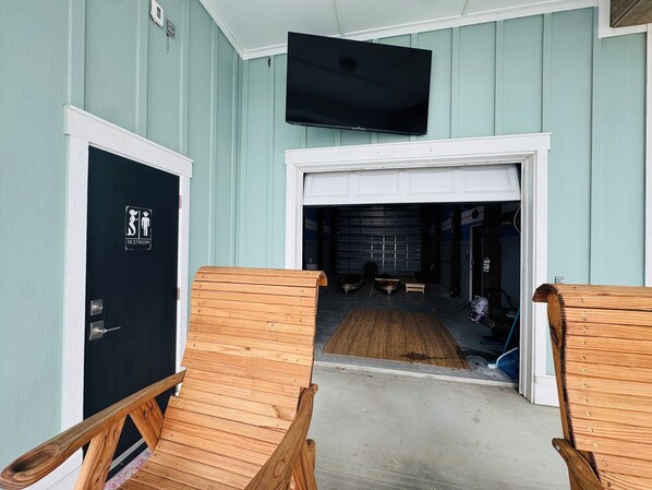 Una habitación con una puerta negra que indica "Restroom", un banco de madera y un televisor montado en la pared.