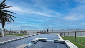 Ein Swimmingpool mit Blick auf das Wasser, eine Palme und eine entfernte Küstenlinie.
