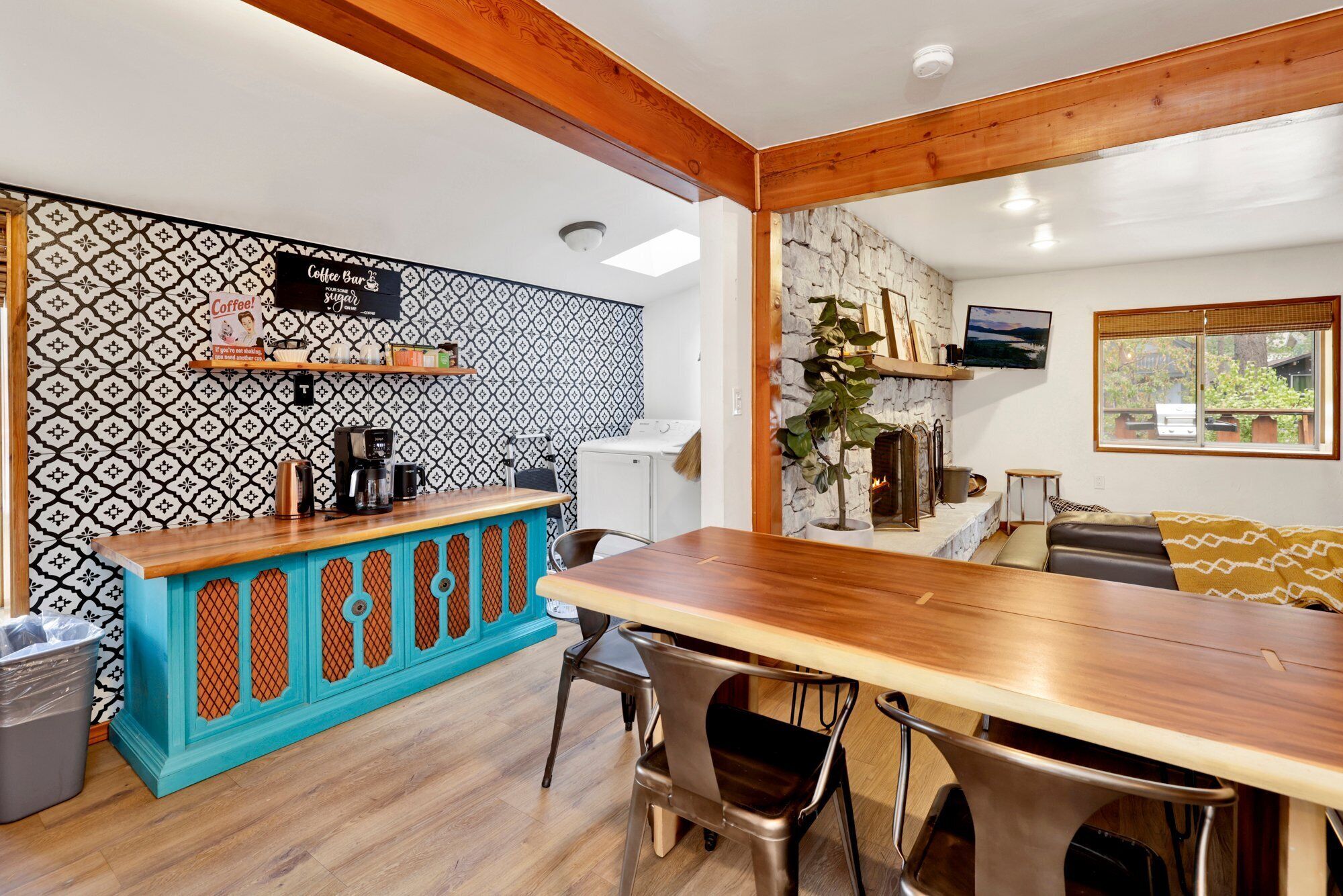 A cozy living area with a wooden dining table, a coffee bar with a patterned backsplash, and a stone fireplace.