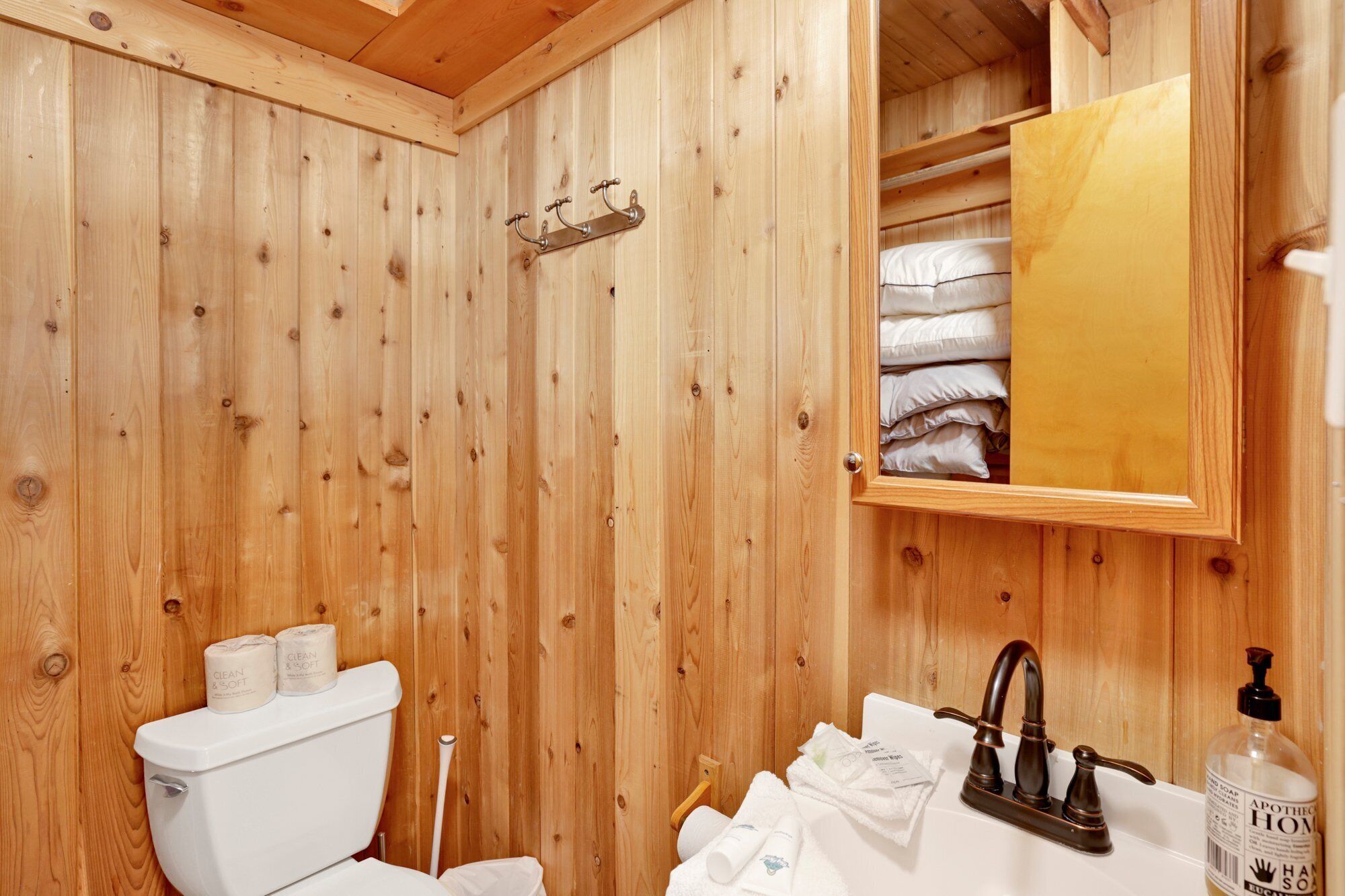 A wooden-paneled bathroom with a toilet, sink, and mirror.