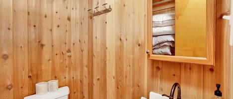 A wooden-paneled bathroom with a toilet, sink, and mirror.