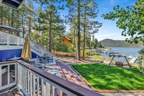 Una terraza con mobiliario exterior, vista a un lago y una casa de madera al fondo.