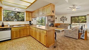 A spacious kitchen with wooden cabinets, a central island, and a fireplace. There is a dining area with a sofa and a table, and a balcony with a view of trees. - Rutter Family Retreat #2482 (Sugarloaf)