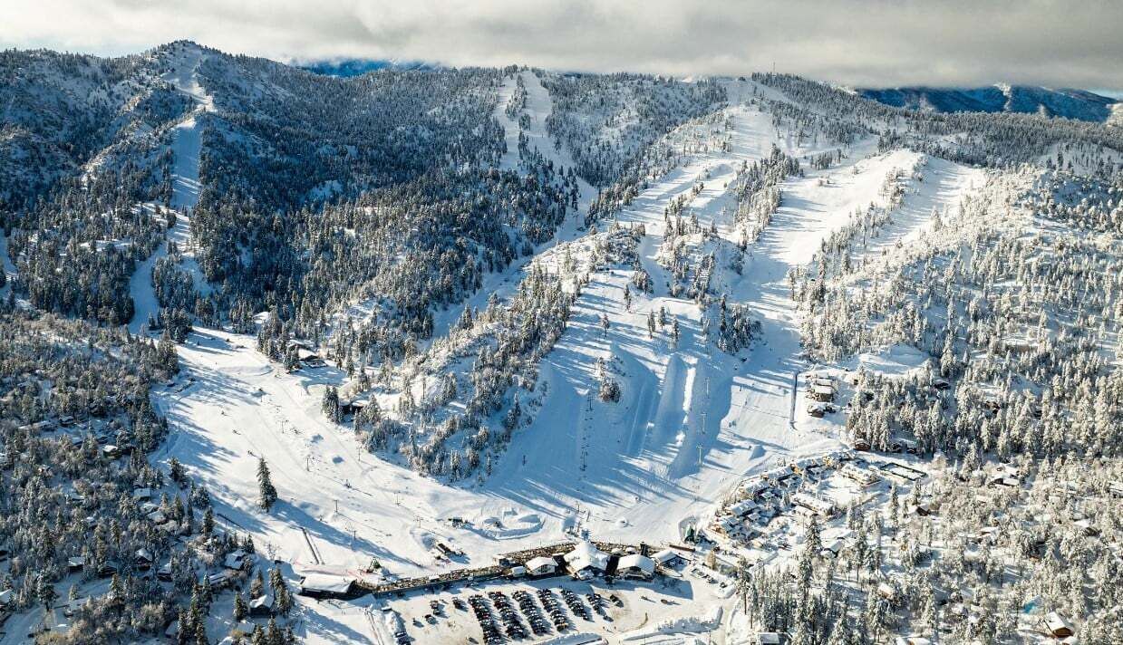 Una località sciistica innevata con piste, rifugi e aree di parcheggio.