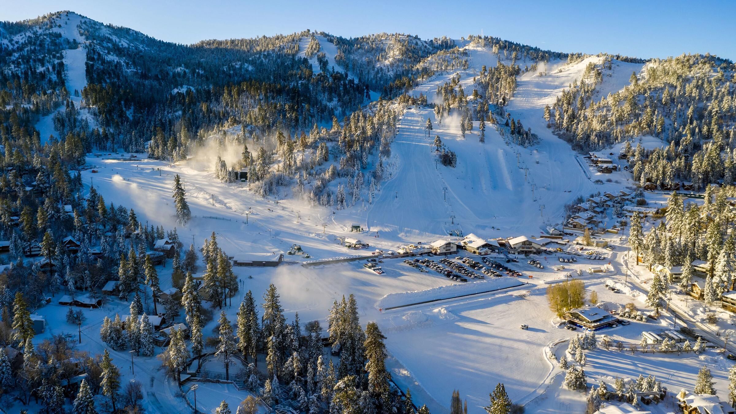 A snow-covered ski resort with multiple ski lifts, buildings, and a mountainous backdrop.