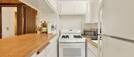 A compact kitchen with white cabinets, a gas stove, a microwave, and a refrigerator.