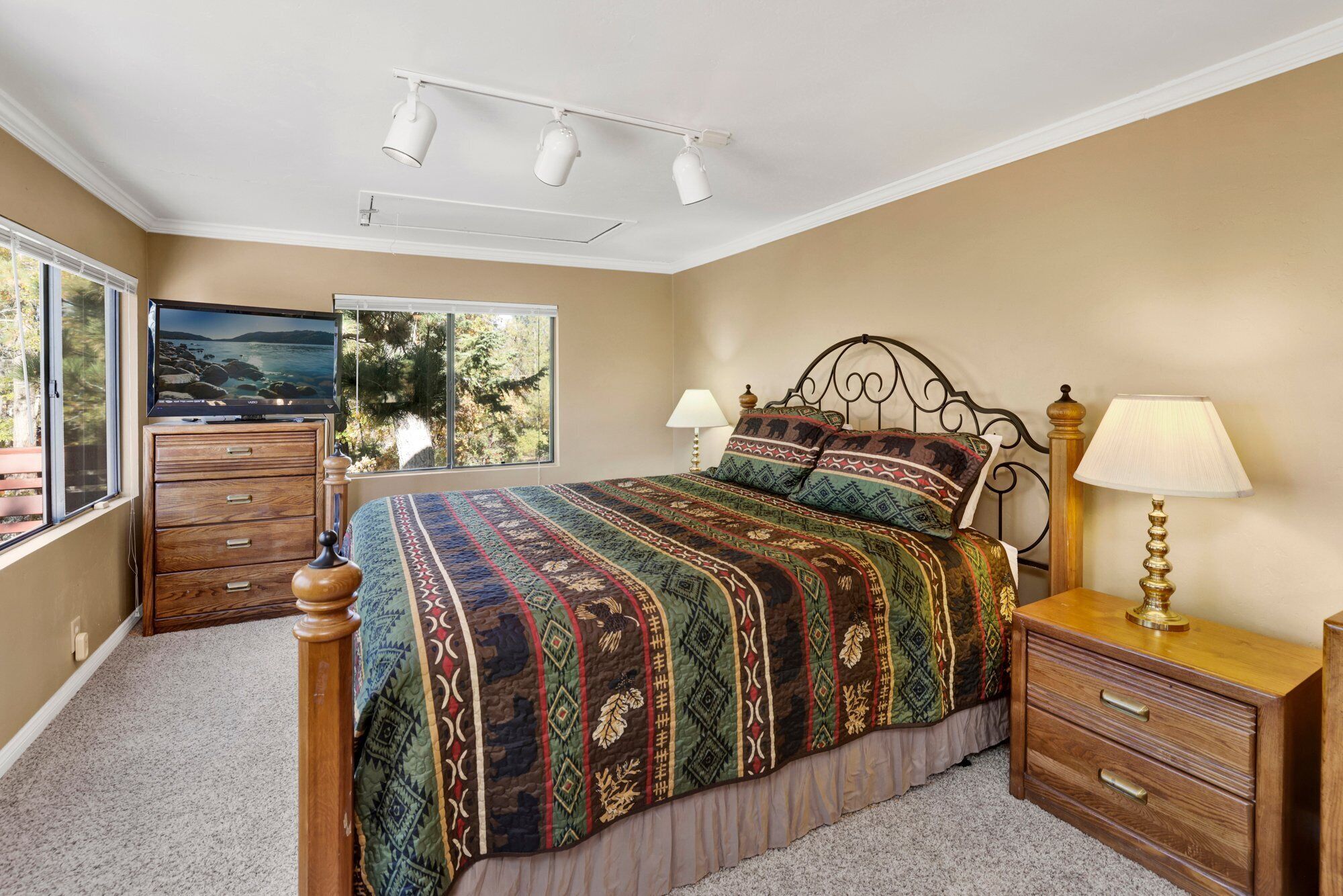 A bedroom with a large bed, a TV on a dresser, a window with a view of trees, and a lamp on a nightstand.