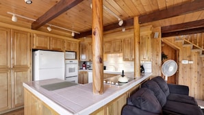 A wooden cabin interior with a kitchen area featuring a refrigerator, microwave, oven, and sink.