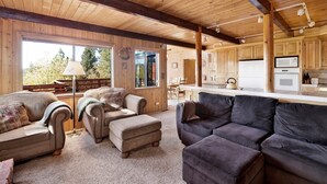 A spacious living area with a large window, wooden ceiling beams, and a kitchen with wooden cabinets.