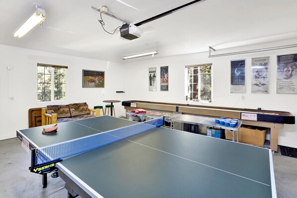 Une table de ping-pong dans une pièce aux murs blancs, avec une fenêtre et des affiches accrochées au mur.
