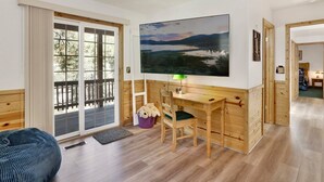 Ein Zimmer mit einem Holztisch, einem Stuhl, einem großen Fenster mit Seeblick und einem Landschaftsbild.