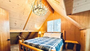 Un dormitorio acogedor en el ático con cama de madera, mesita de noche y un original candelabro de astas.