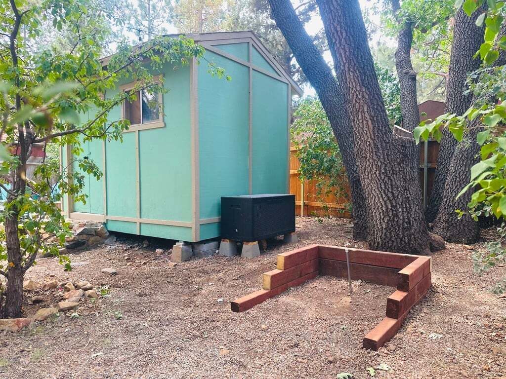Una petita caseta de blau clar amb un altaveu negre al davant, envoltada d'arbres i una tanca de fusta.