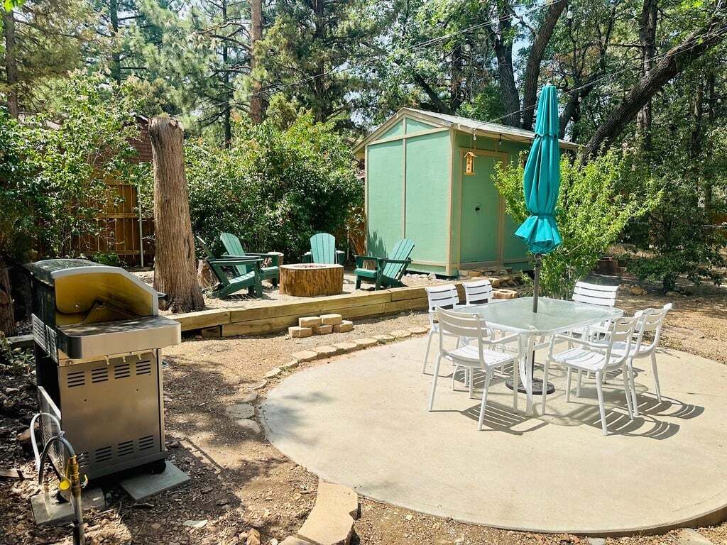 A patio with a round table and chairs, a green shed, and a grill.