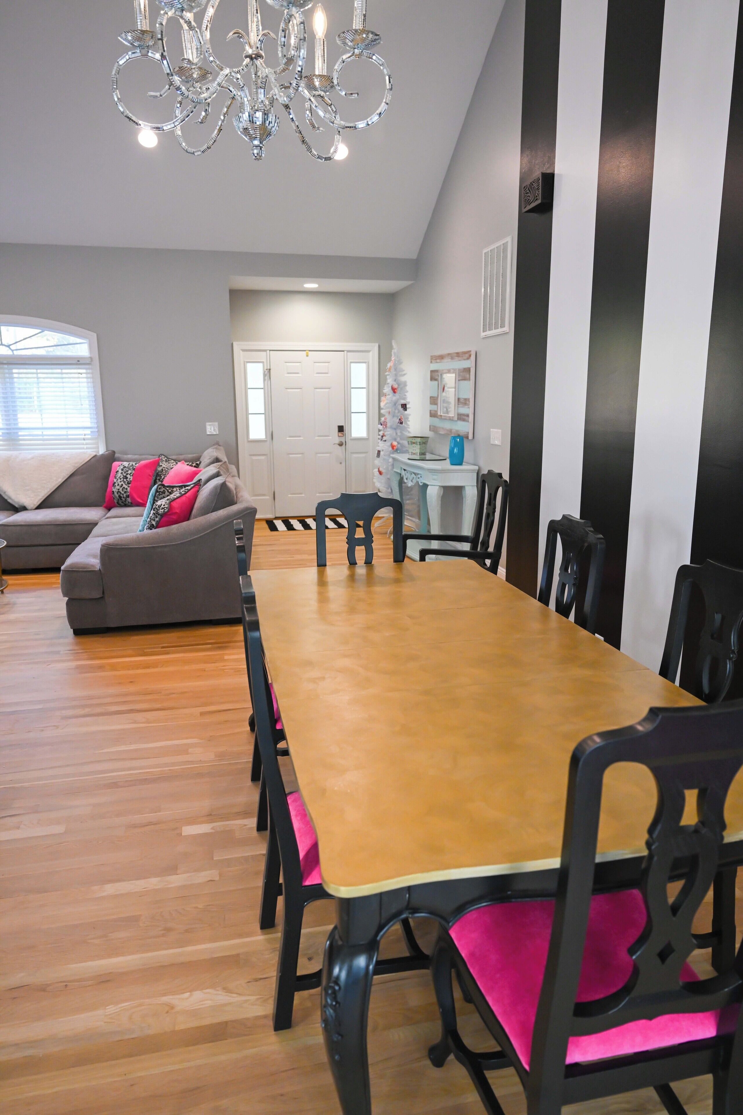 A dining area with a long wooden table, black chairs with pink cushions, and a chandelier.