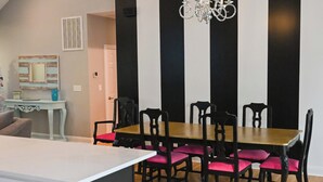 Un coin repas avec une table en bois et des chaises noires, un lustre et un buffet blanc.