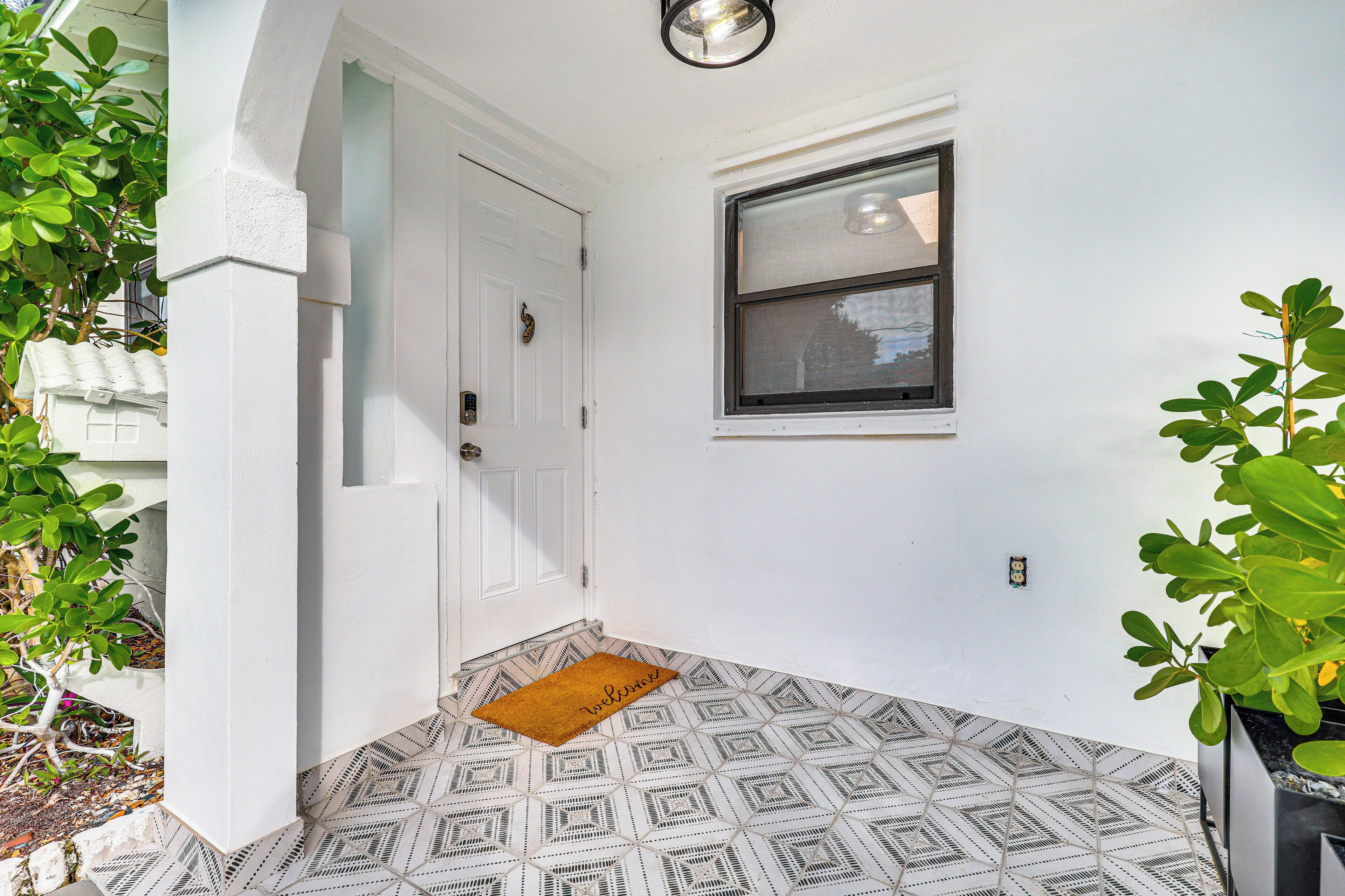 A clean, white-walled entrance with a geometric patterned floor, a small window, and a welcome mat.