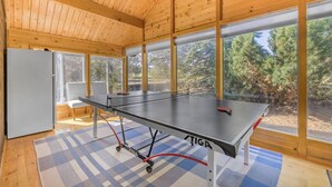 A ping pong table in a room with large windows, wooden walls, and a checkered floor. - Come stay at the Moose Jam! (Island Park)