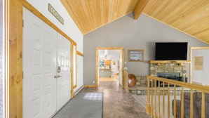 A hallway with a wooden ceiling, a stone fireplace, and a television mounted on the wall. - Come stay at the Moose Jam! (Island Park)