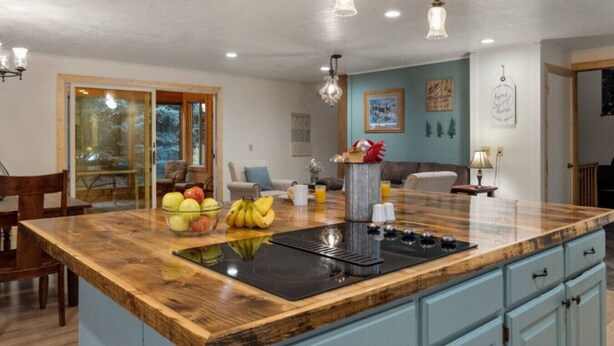 A kitchen with a central island, wooden cabinets, and a dining area with a table and chairs. - Come stay at the Moose Jam! (Island Park)