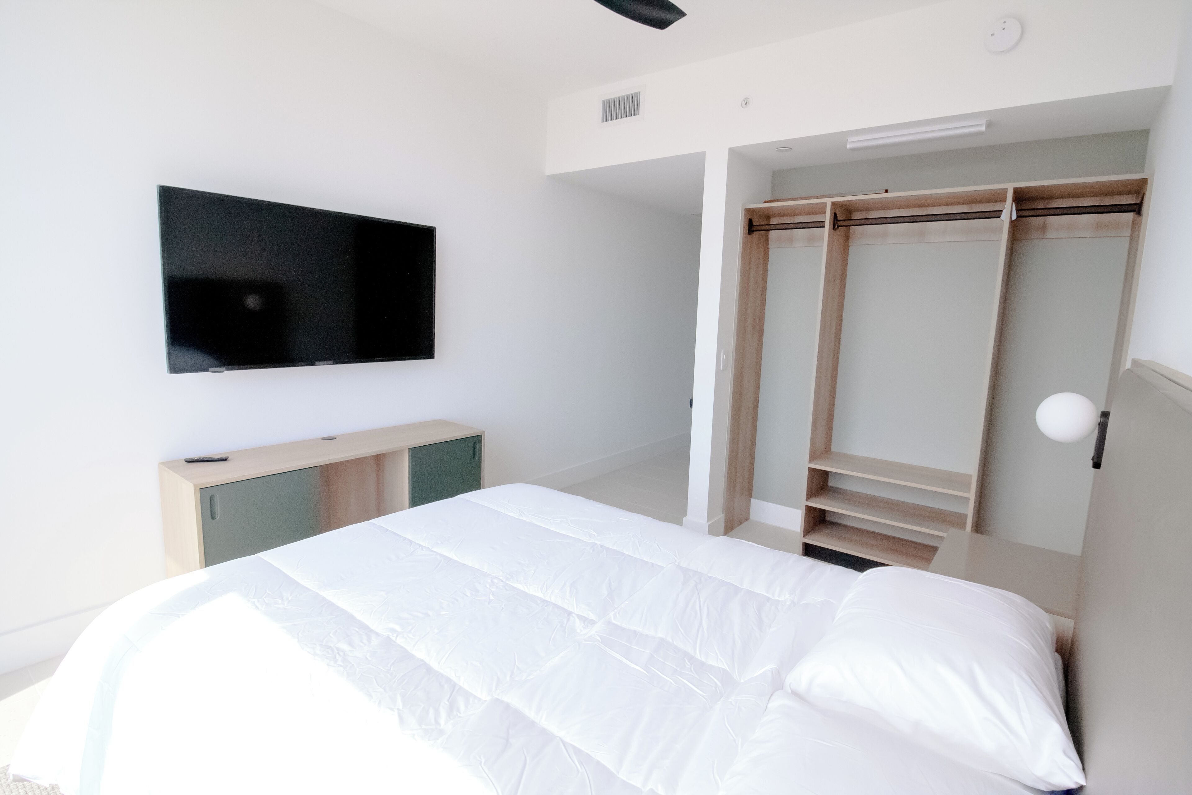 Une chambre à coucher avec un lit, un téléviseur fixé au mur et un dressing.
