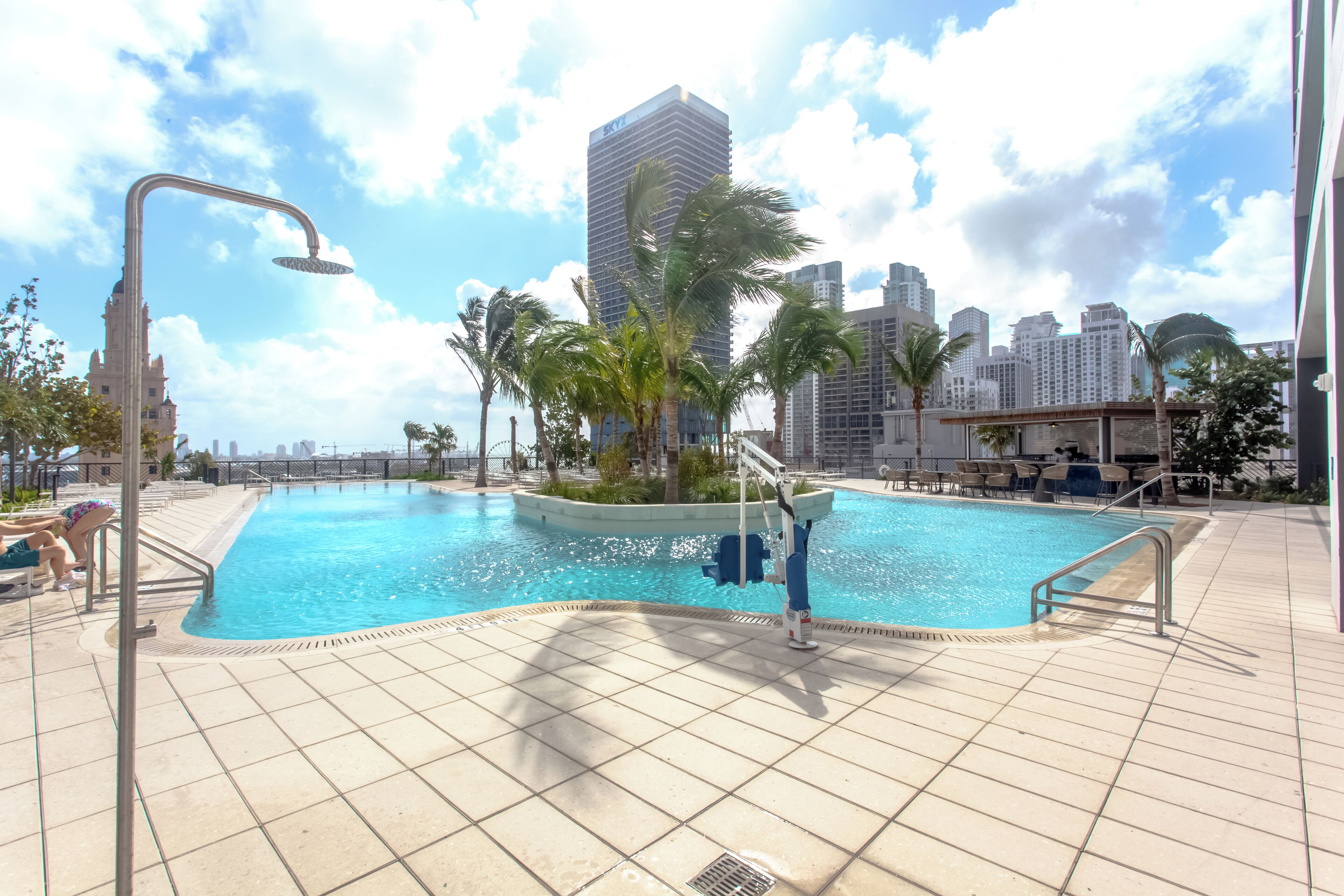 A swimming pool with a city skyline in the background, surrounded by palm trees and a tiled deck.
