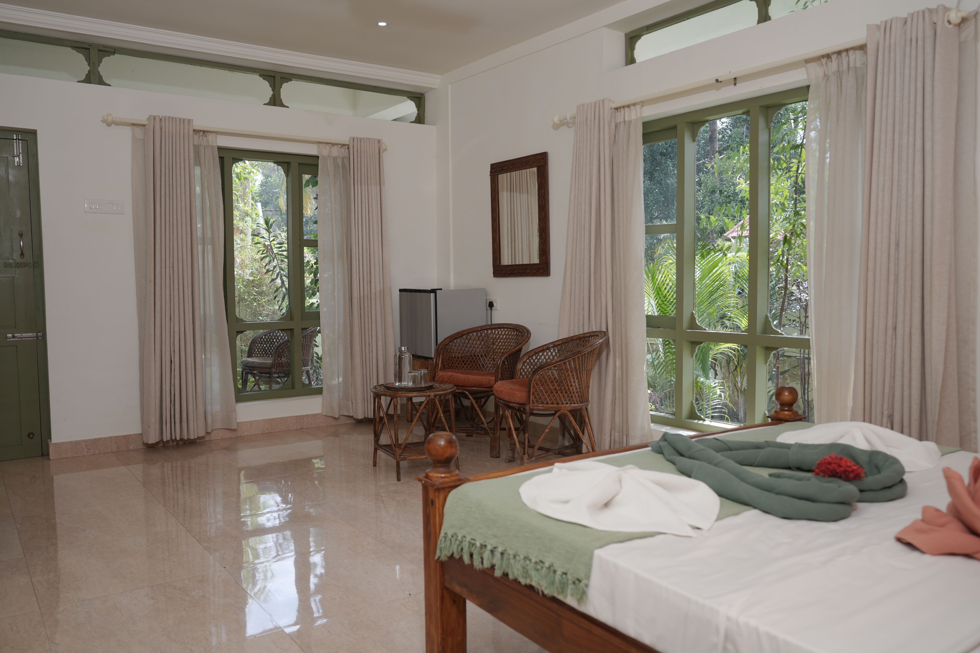A room with a bed, a desk, two chairs, and large windows.