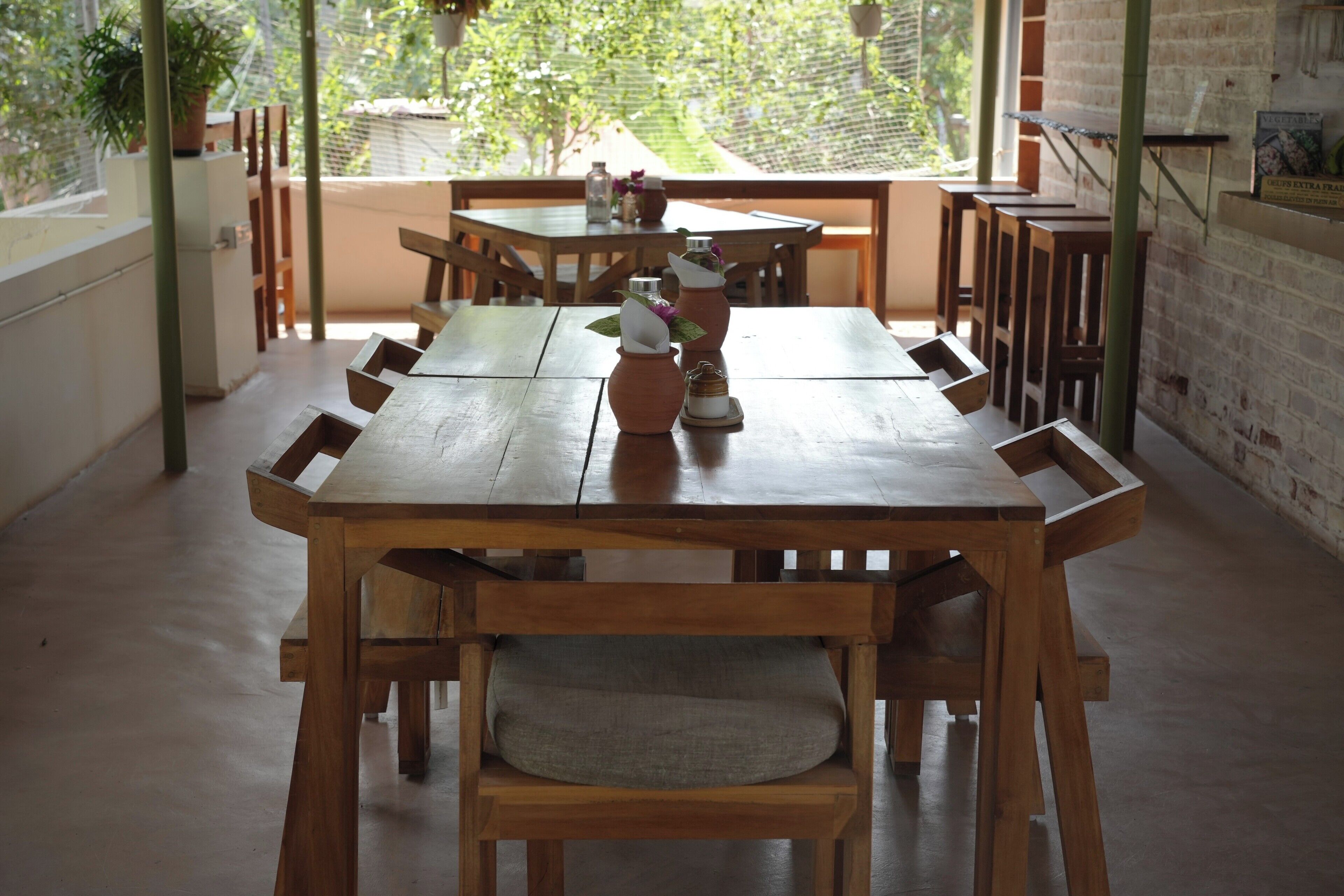 Una mesa de madera con sillas, una planta en maceta y un muro de ladrillo.
