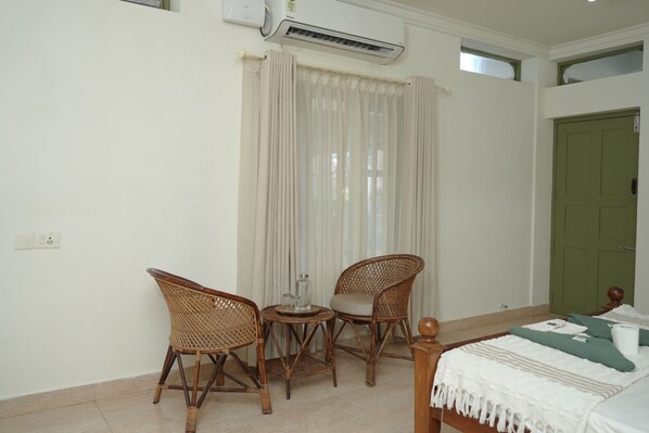 A room with a bed, two wicker chairs, a small round table, and a window with curtains. - Ashiyana Cliff & Beach Resort by Onespace (Varkala)