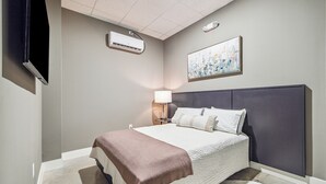 A hotel room with a bed, a bedside lamp, a painting on the wall, and an air conditioning unit. - Centrally located, unique and brand new condo (Houston)