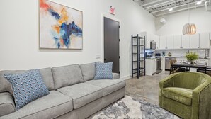 A modern living room with a grey sofa, patterned cushions, a green armchair, and a large abstract painting on the wall. - Centrally located, unique and brand new condo (Houston)